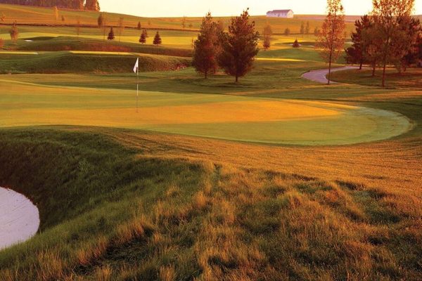 A Somerby green at sunset, framed by prairie grass and a deep bunker in the foreground