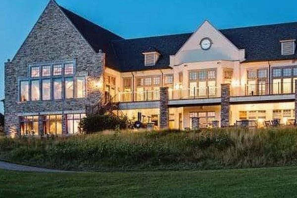 The stone gable of the Clubhouse in the evening, its dining room windows lit from within