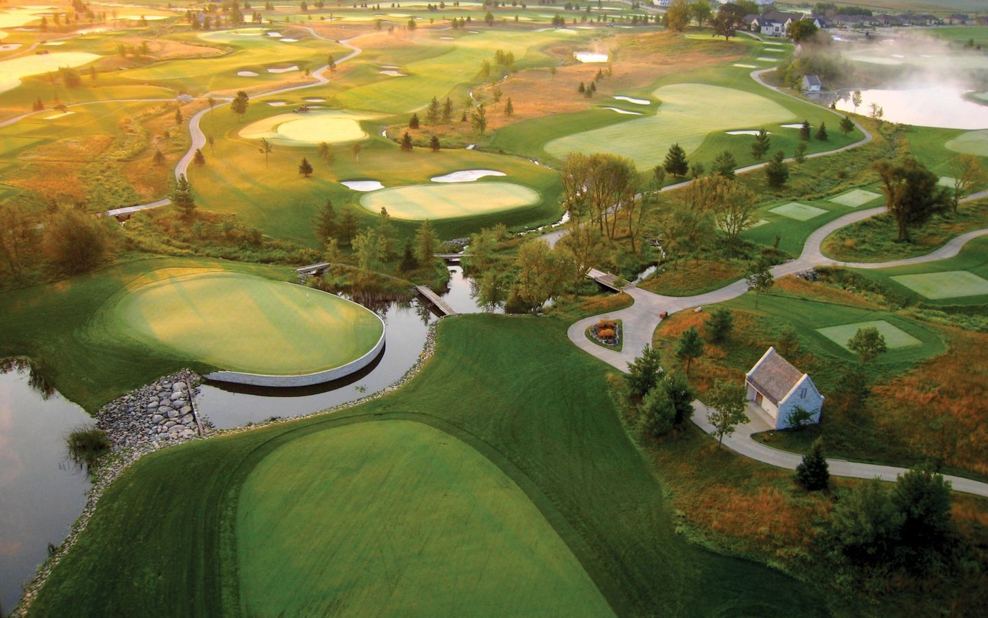 The Somerby course at dawn, seen from the air, with mist over the water and the greens laid out along a winding creek